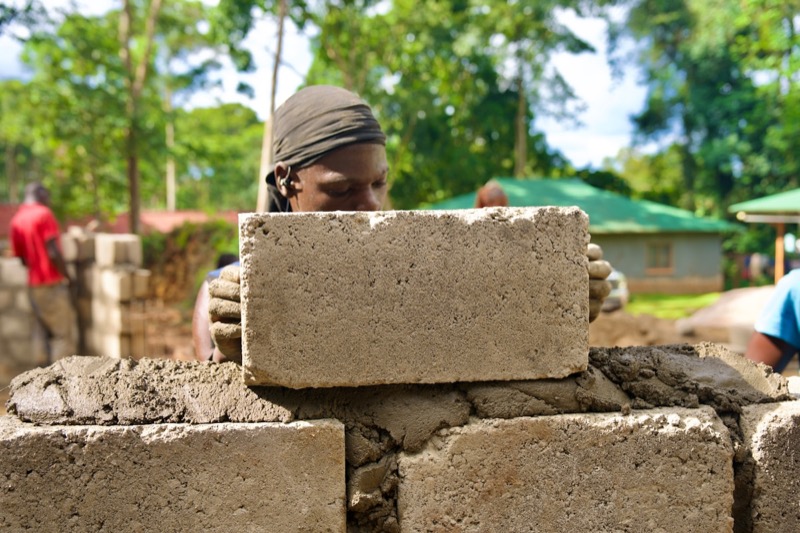 A Ugandan mason settling a fresh course of concrete blocks at a residential site.